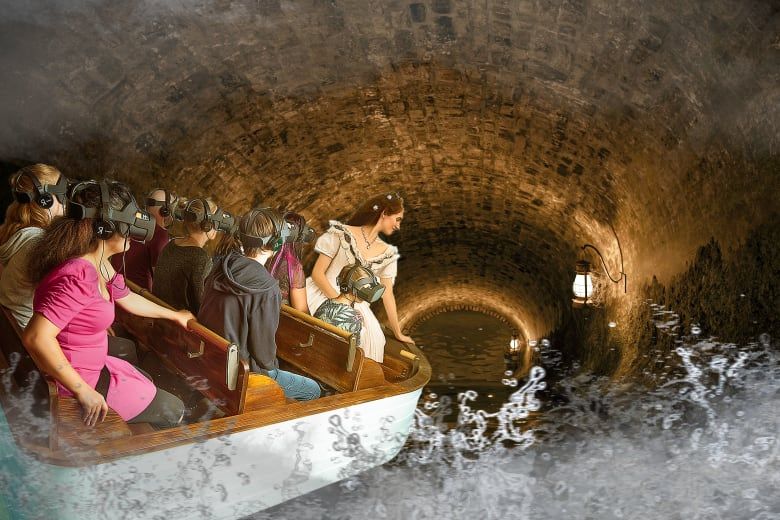 Visitors in VR headsets riding a boat through a stone tunnel alongside an actress in period Victorian dress.