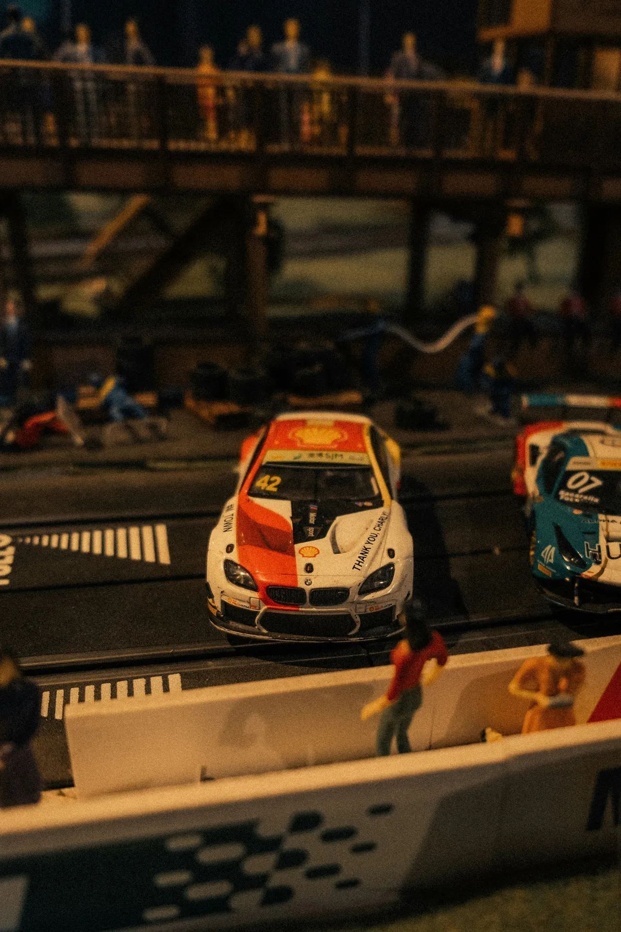 Two miniature electric slot cars, one red and one blue, racing side-by-side on a plastic track.