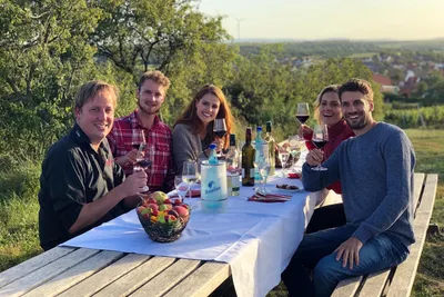 Smiling group of friends sitting at a table in the vineyard with wine glasses in the evening sun
