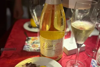 Bottle of winemaker's sparkling wine with a filled glass and a small plate of finger food on a red tablecloth
