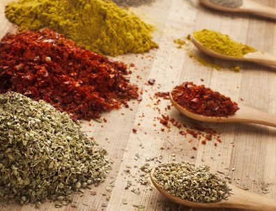 Ground spices and dried herbs on wooden spoons and a wooden board