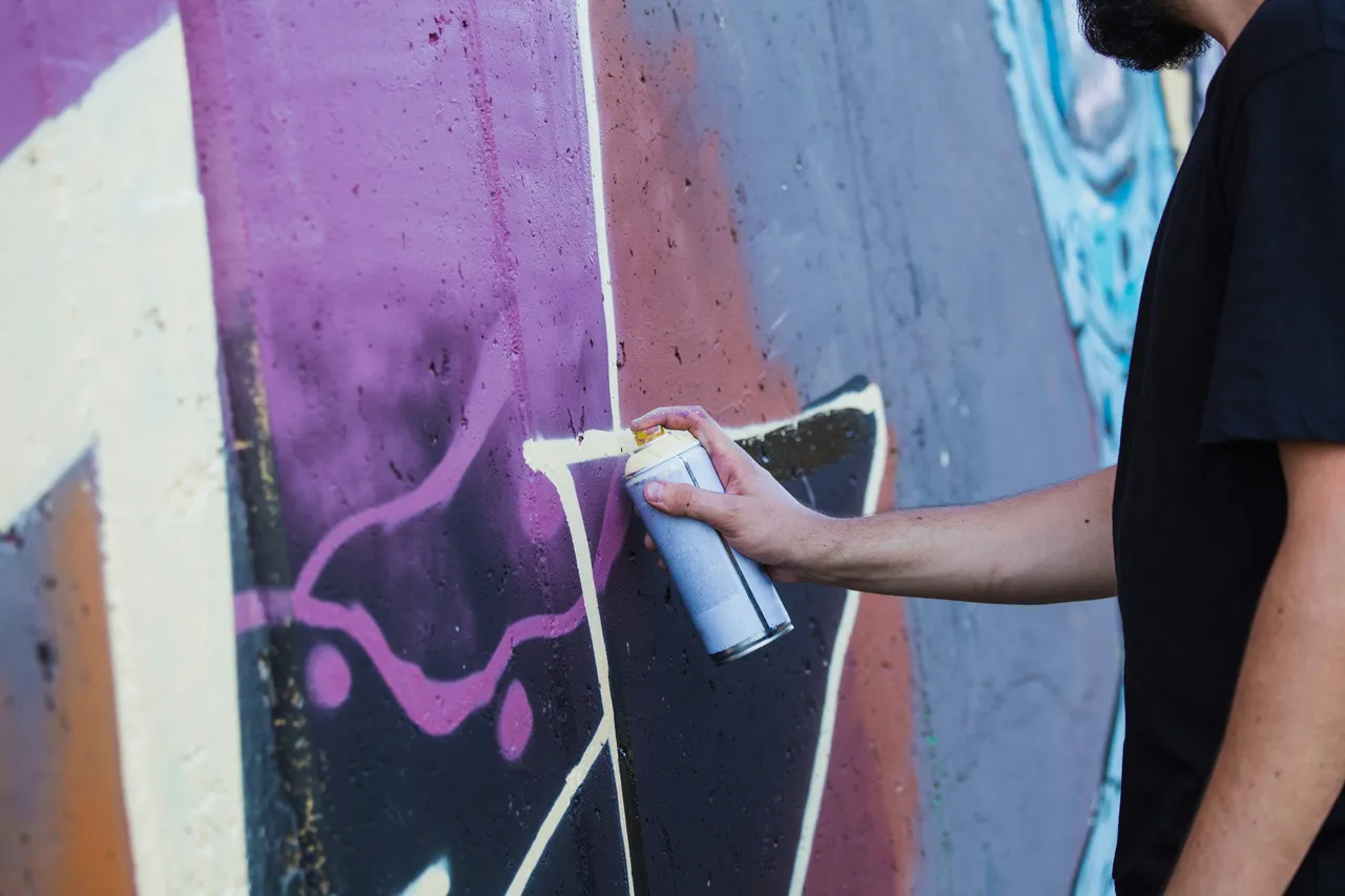 Close-up of a hand spray painting purple details onto a graffiti mural