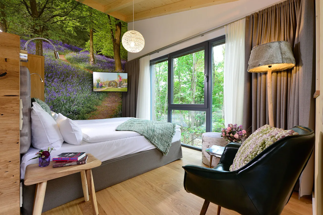 Bright tree chalet room with panoramic window, armchair and bed overlooking the forest