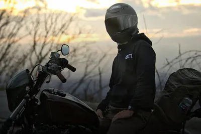 Motorcycle riding: rider in a helmet next to a motorcycle at sunset