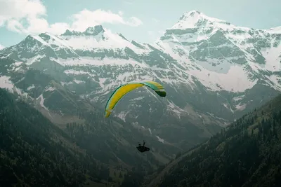 Paragliding: paraglider flying over snow-capped mountains