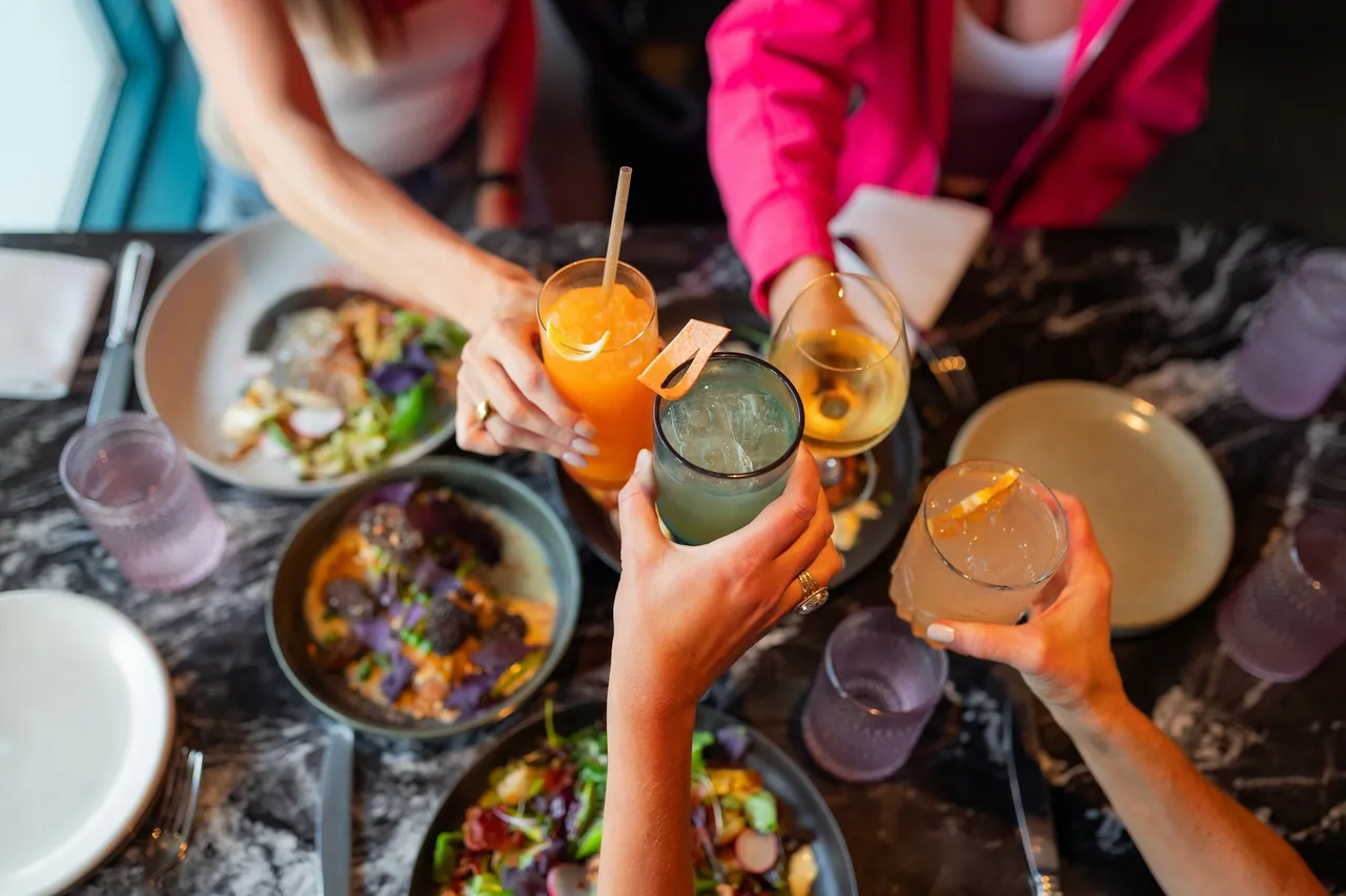 Friends toasting with colourful cocktails and wine over a table of shared dishes