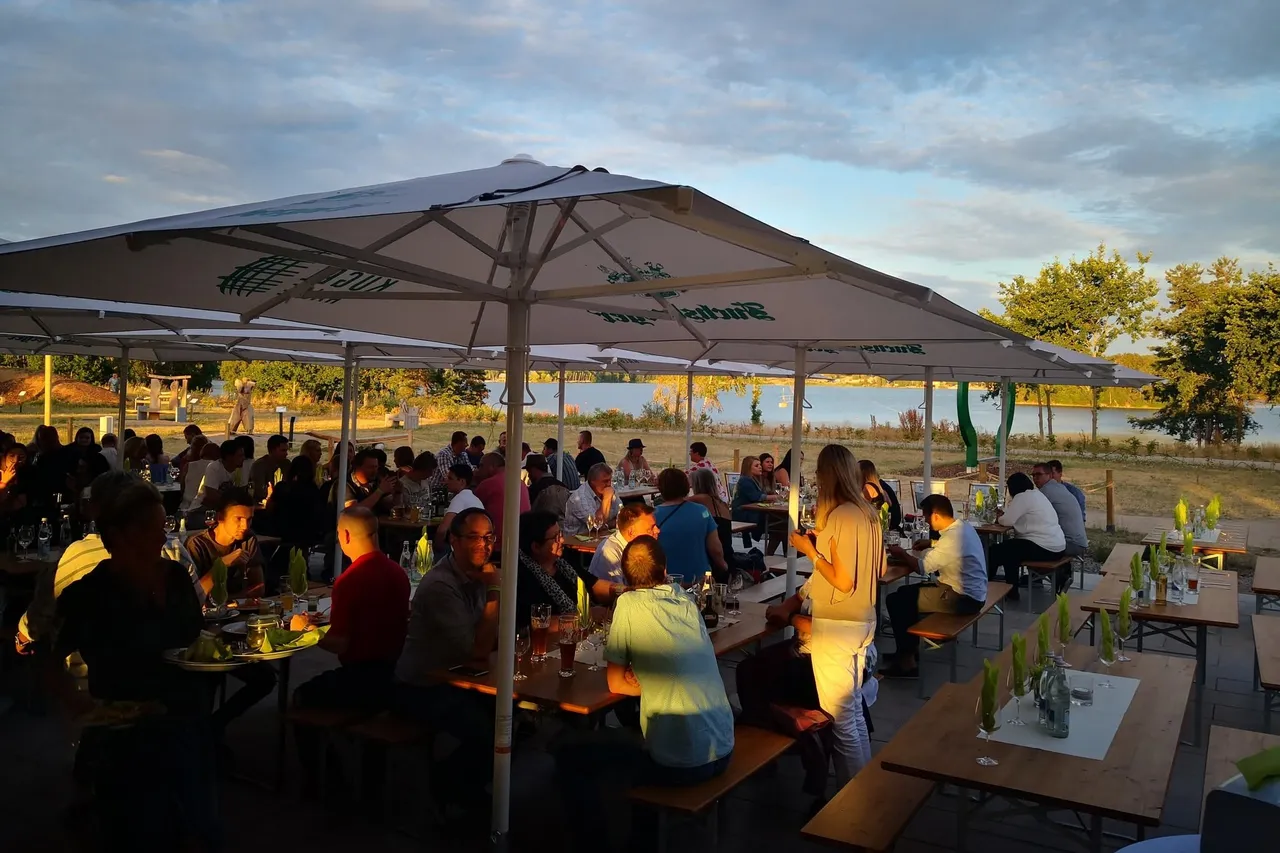 Lakeside garden restaurant with guests sitting under large white umbrellas