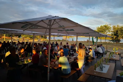 Lakeside garden restaurant with guests sitting under large white umbrellas