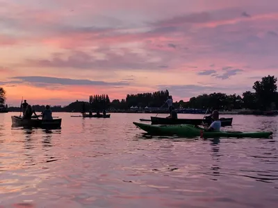 Canoes and kayaks silhouetted on calm water under a pink sunset sky in Berlin