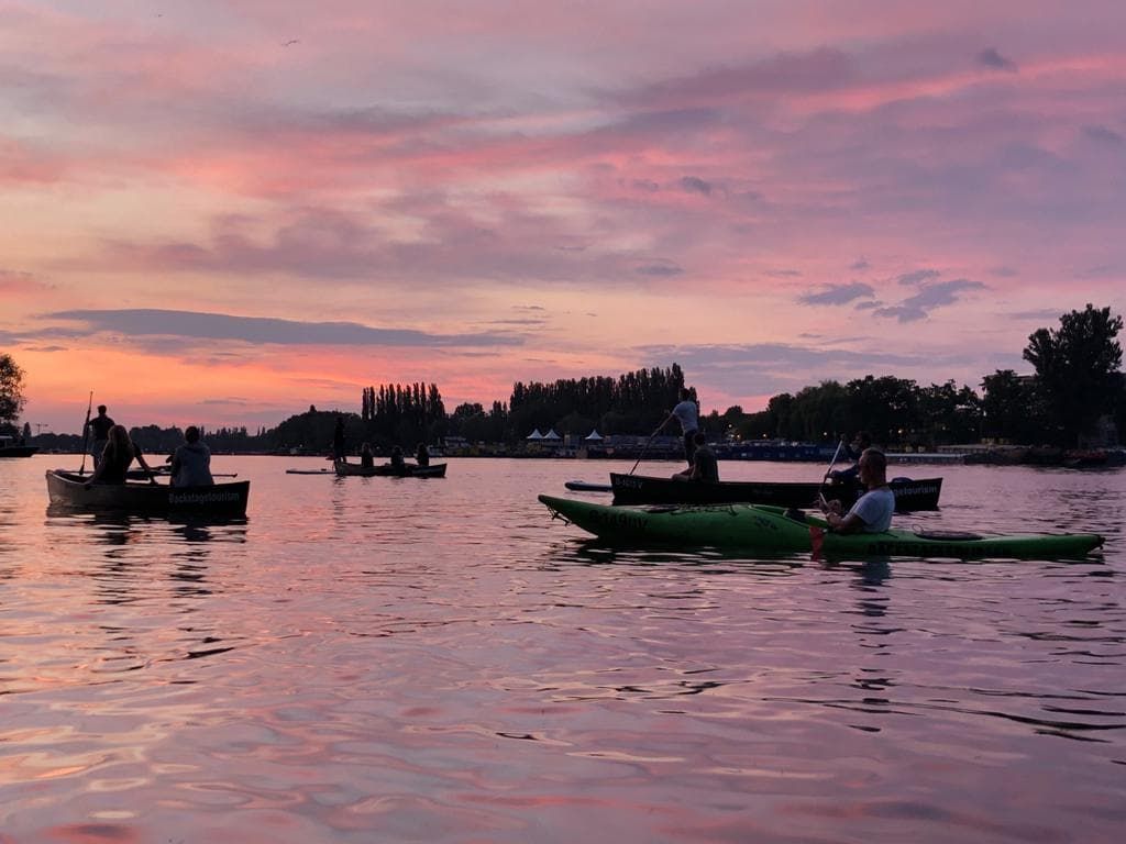 Canoes and kayaks silhouetted on calm water under a pink sunset sky in Berlin
