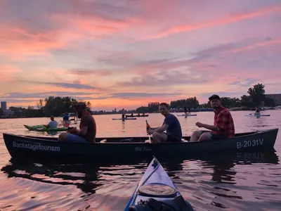 Paddlers relaxing in a canoe on the Spree in Berlin under a pink and purple sunset sky