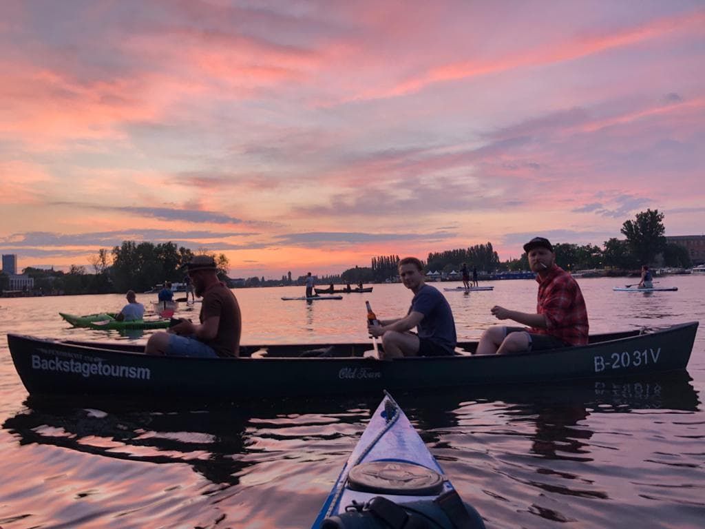 Paddlers relaxing in a canoe on the Spree in Berlin under a pink and purple sunset sky