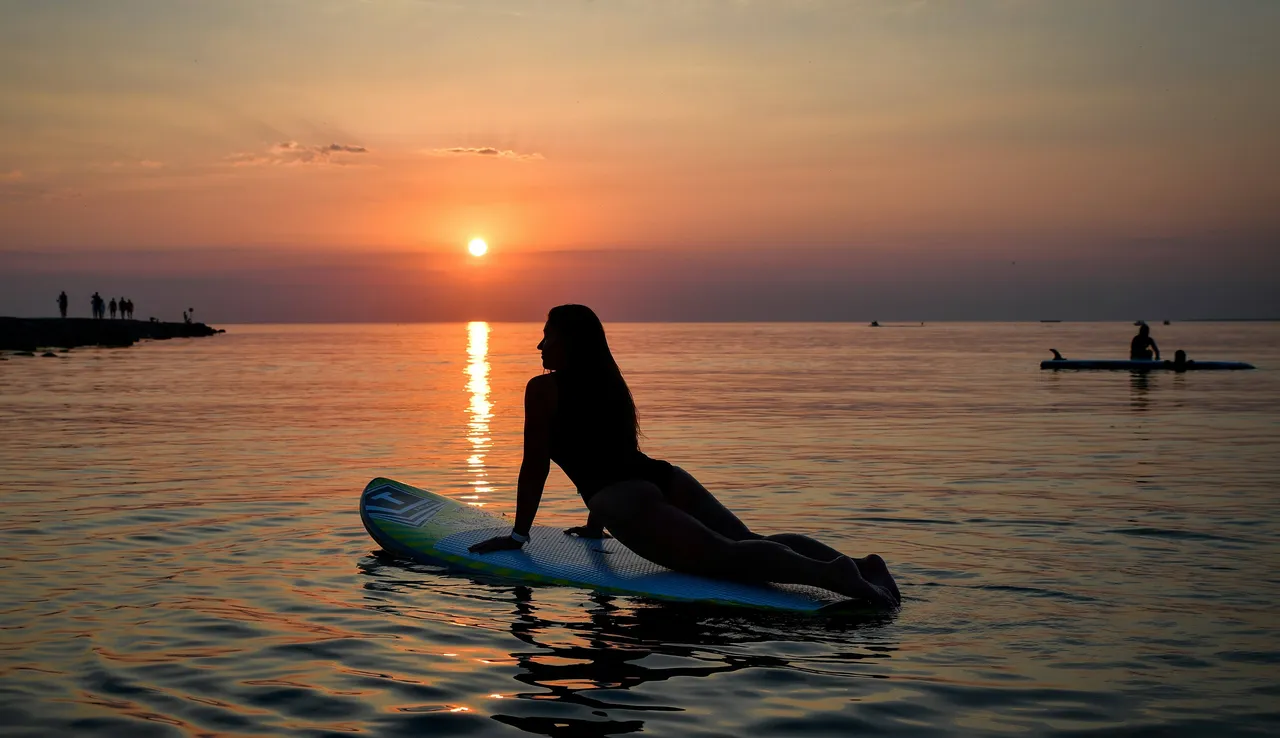 A person doing yoga on a SUP board at sunset