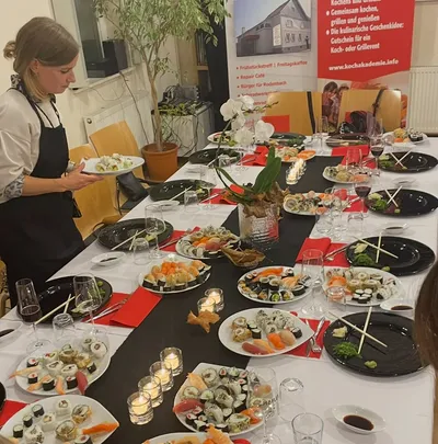 Long dinner table set with homemade sushi platters, wine glasses and candles
