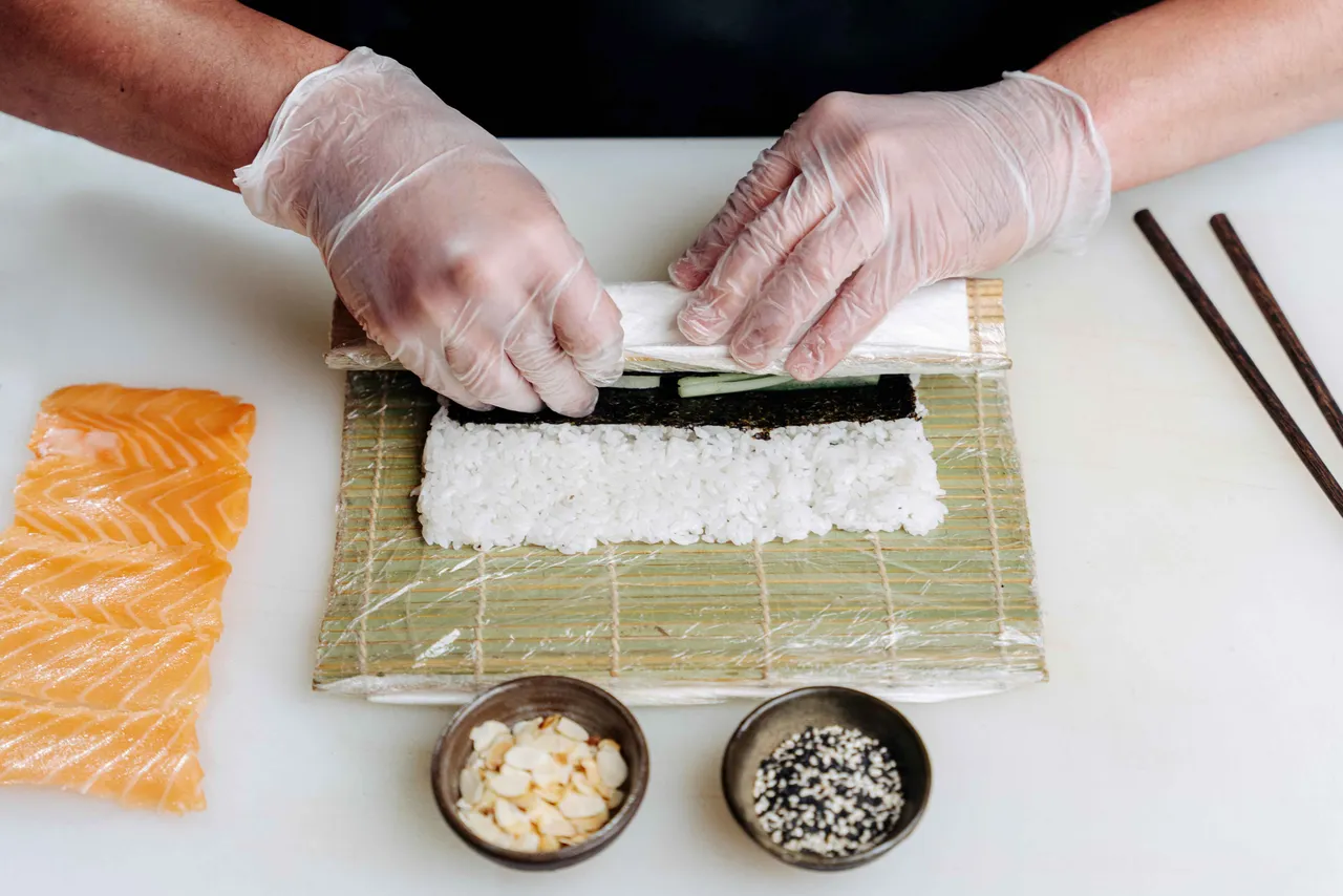 A person rolling sushi on a mat