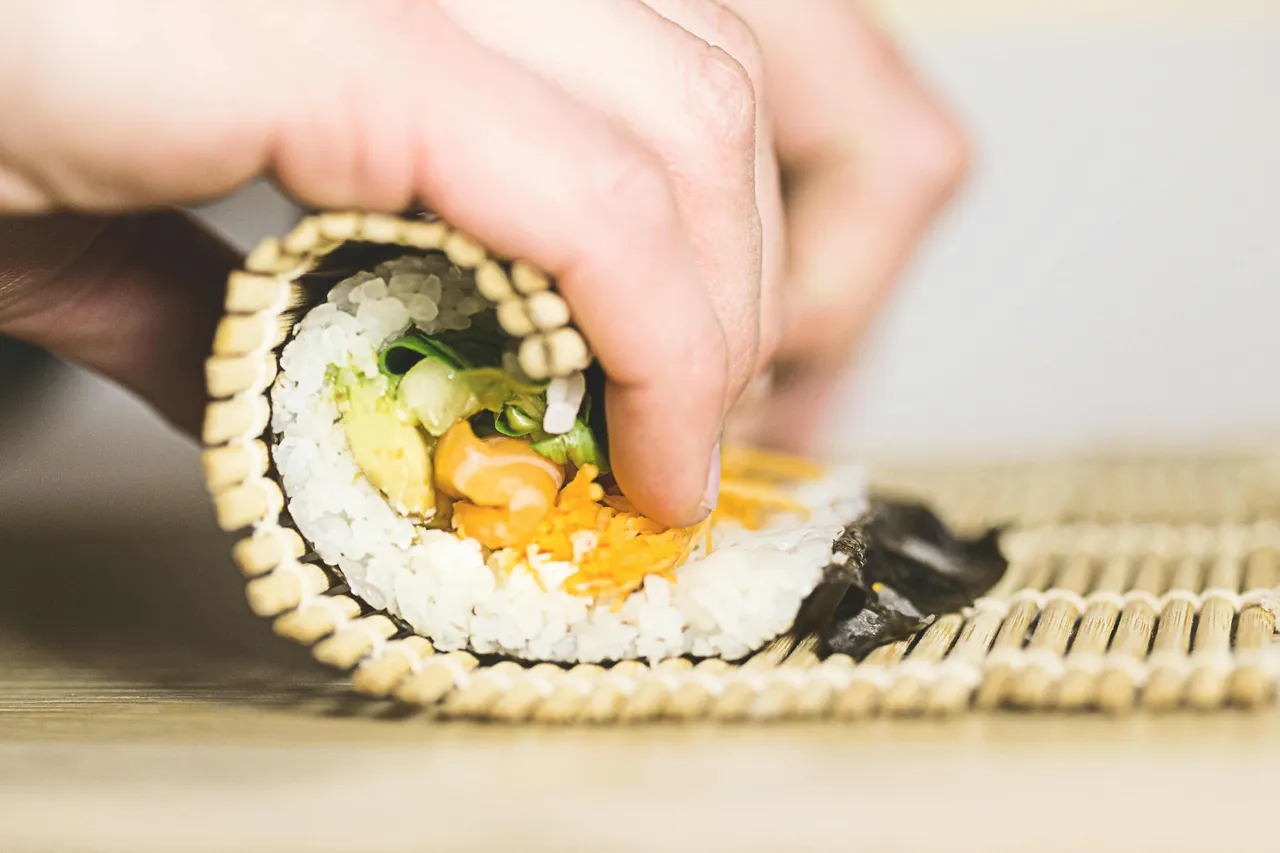 A person rolling sushi on a mat