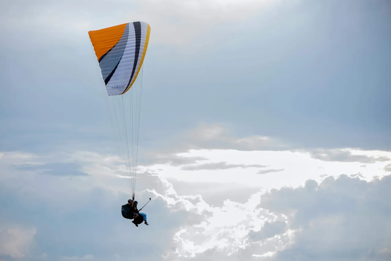 Tandem paraglider with pilot and passenger flying above a layer of clouds