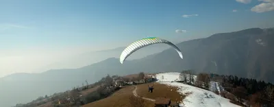 Paraglider gliding over a hilly landscape with patches of snow