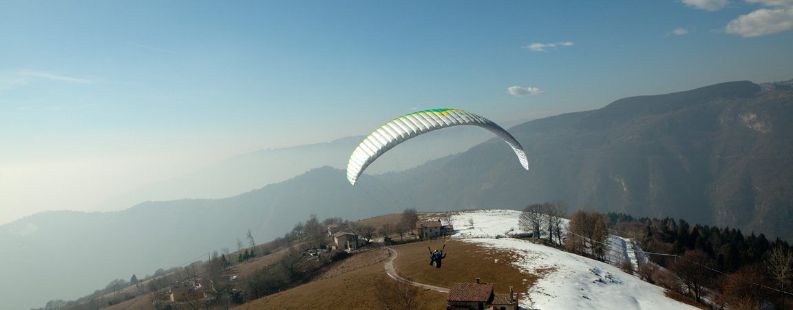 Paraglider gliding over a hilly landscape with patches of snow