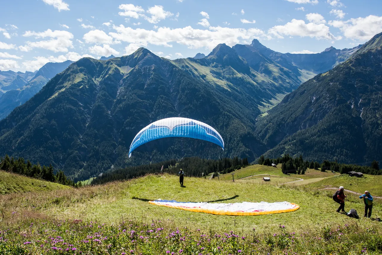 Paraglider launching from an alpine meadow with a mountain panorama in the background