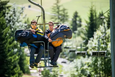 Two paragliders with their gear riding a chairlift up the mountain