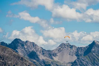 Paraglider soaring above rugged alpine peaks under a blue sky