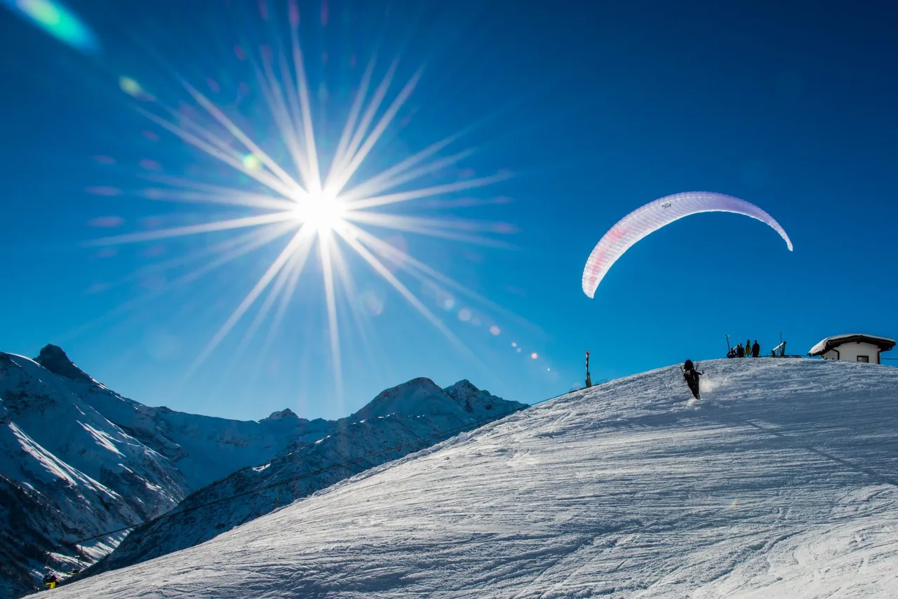 Paraglider taking off above a snowy mountain slope in bright winter sunshine