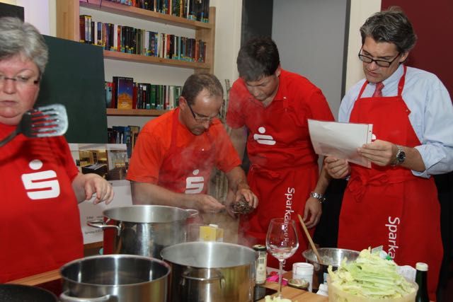 People in red aprons cooking together and following a recipe at the stove