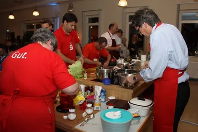 A group of people preparing food at several kitchen stations