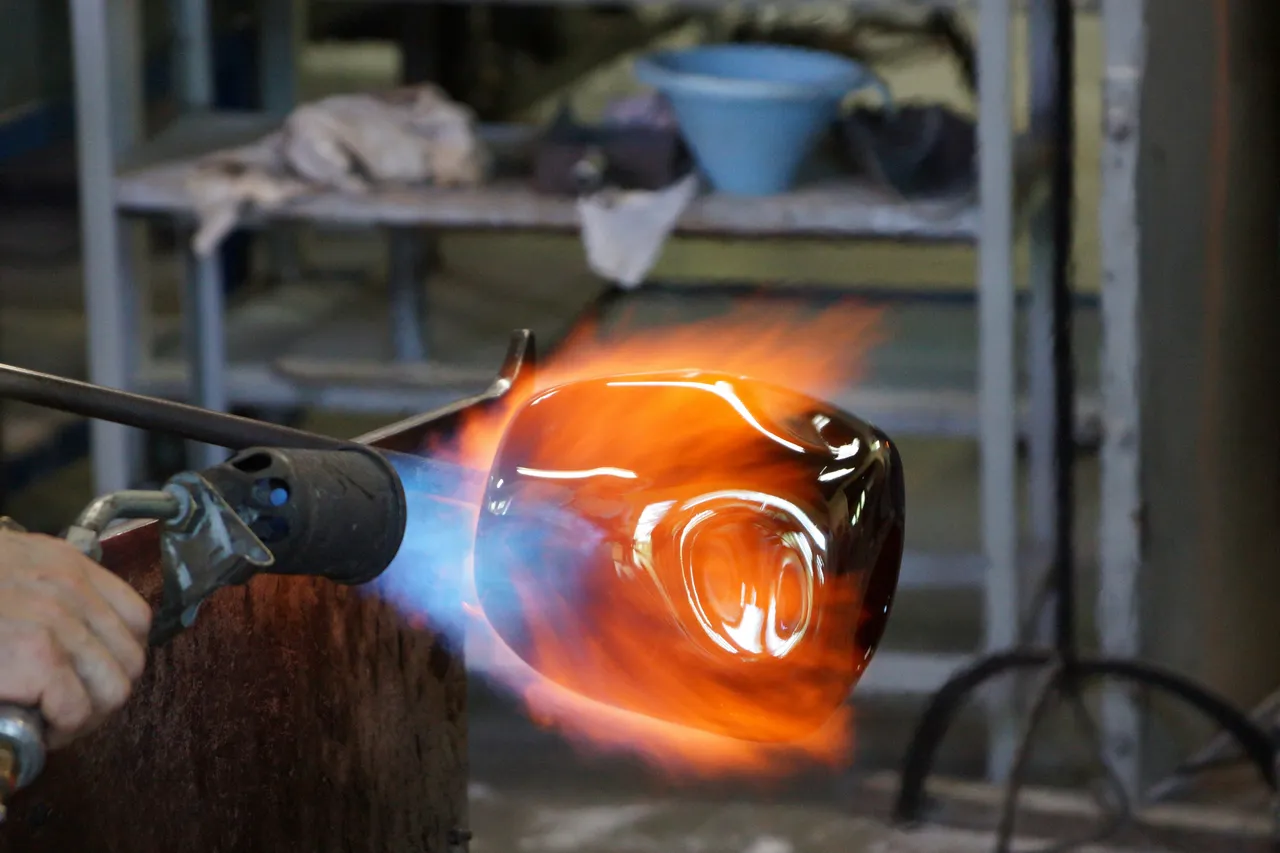 Close-up of a torch flame melting a glass vessel that glows bright orange