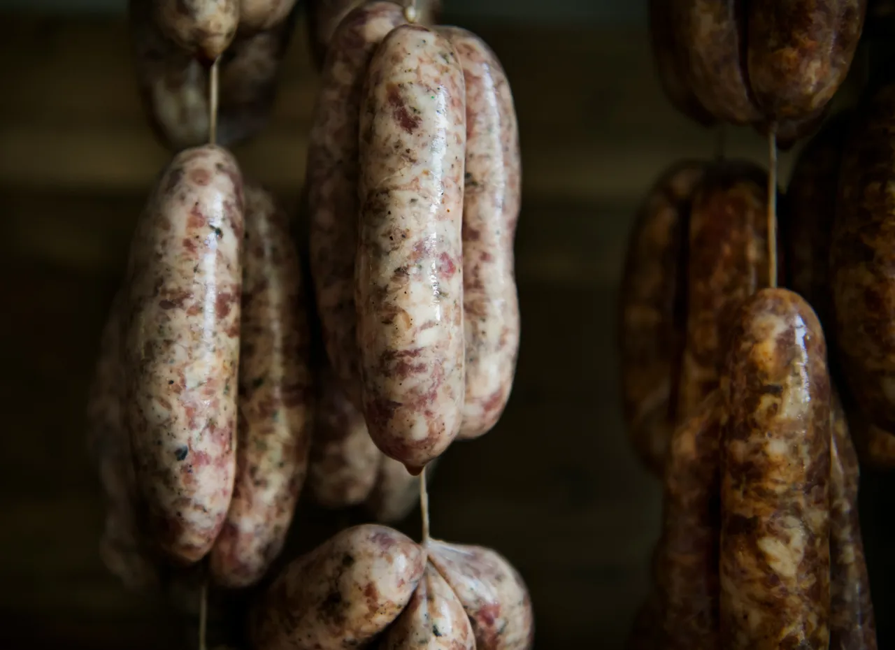 Raw sausage links tied with twine resting on a rustic wooden table covered in scattered flour.