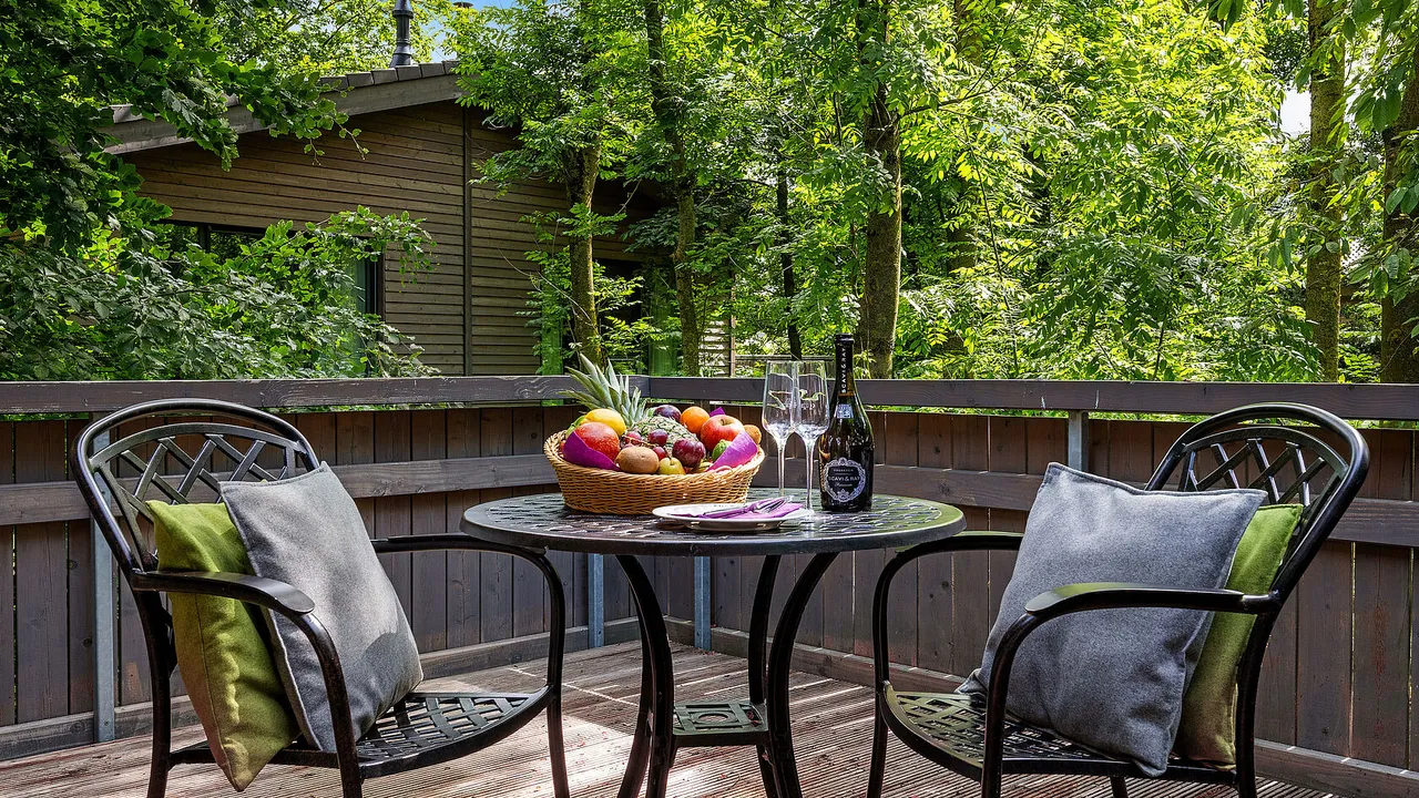 Private chalet terrace with two chairs, cushions and a fruit bowl surrounded by green treetops