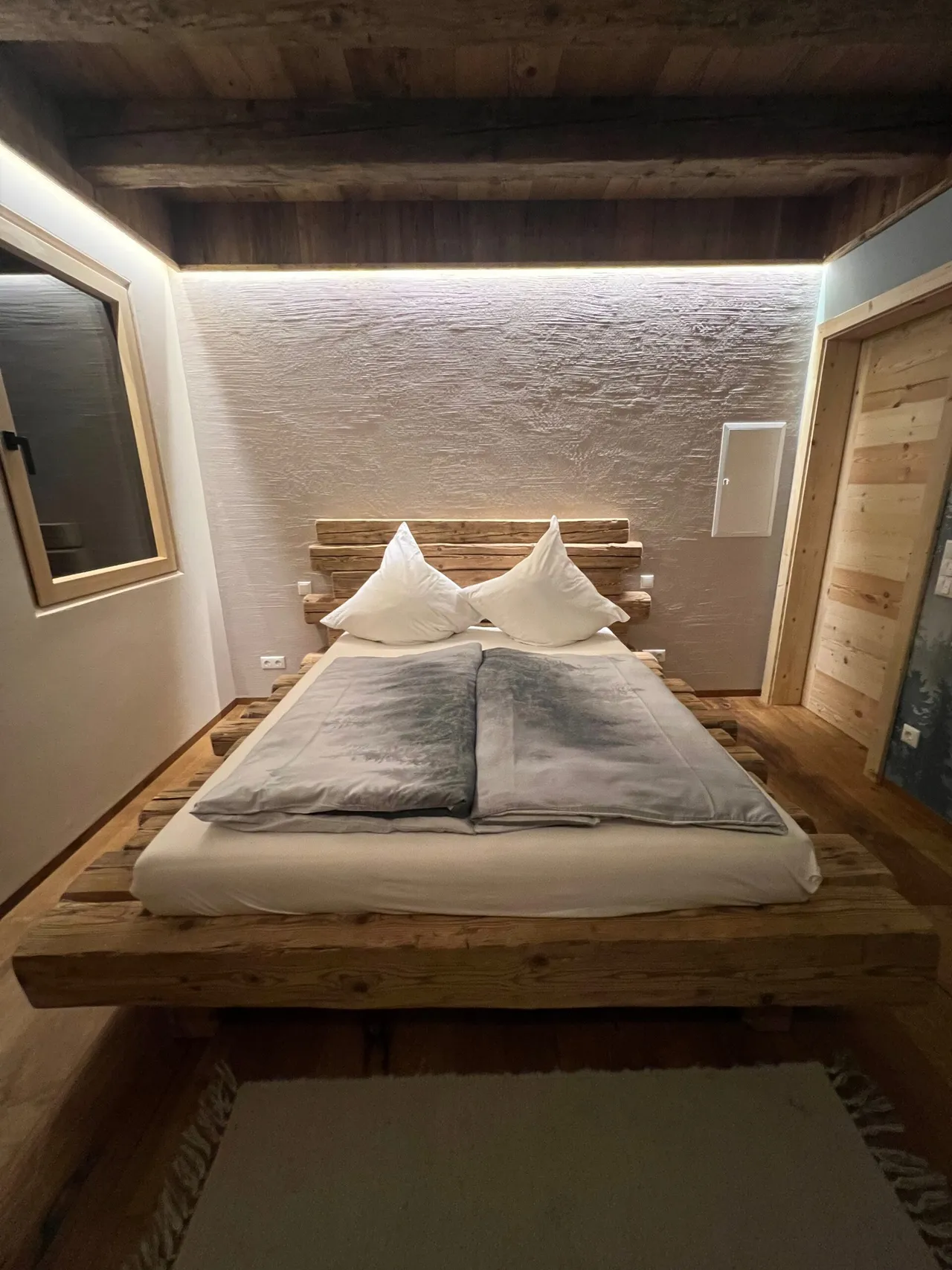 Cozy treehouse bedroom with a solid wood double bed, backlit stone wall and rustic wooden ceiling in the Bavarian Forest
