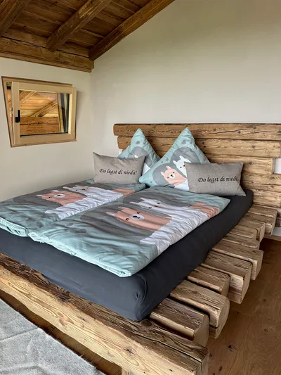 Double bed made of rustic wooden beams with alpaca-themed pillows and bedding under a sloped wooden roof