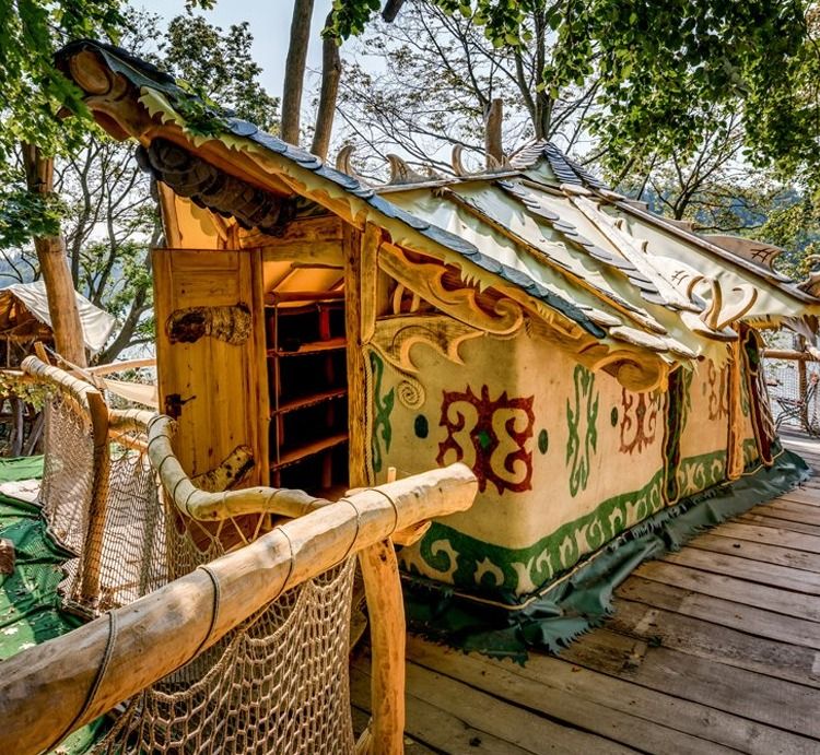 Treehouse yurt with felt ornaments and carved wooden roof on a wooden deck among trees at the Kriebstein reservoir