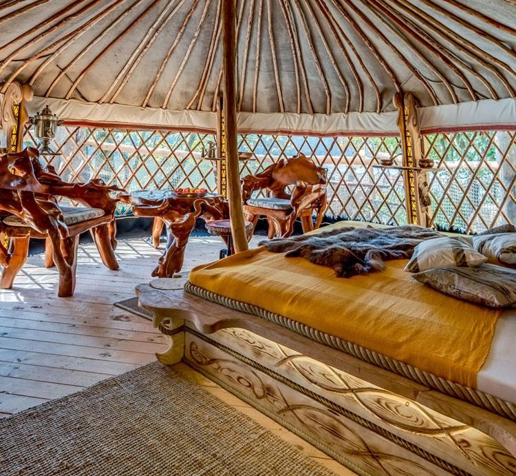 Inside a treehouse yurt with a giant larch wood bed, fur throw and mangrove root table and armchairs