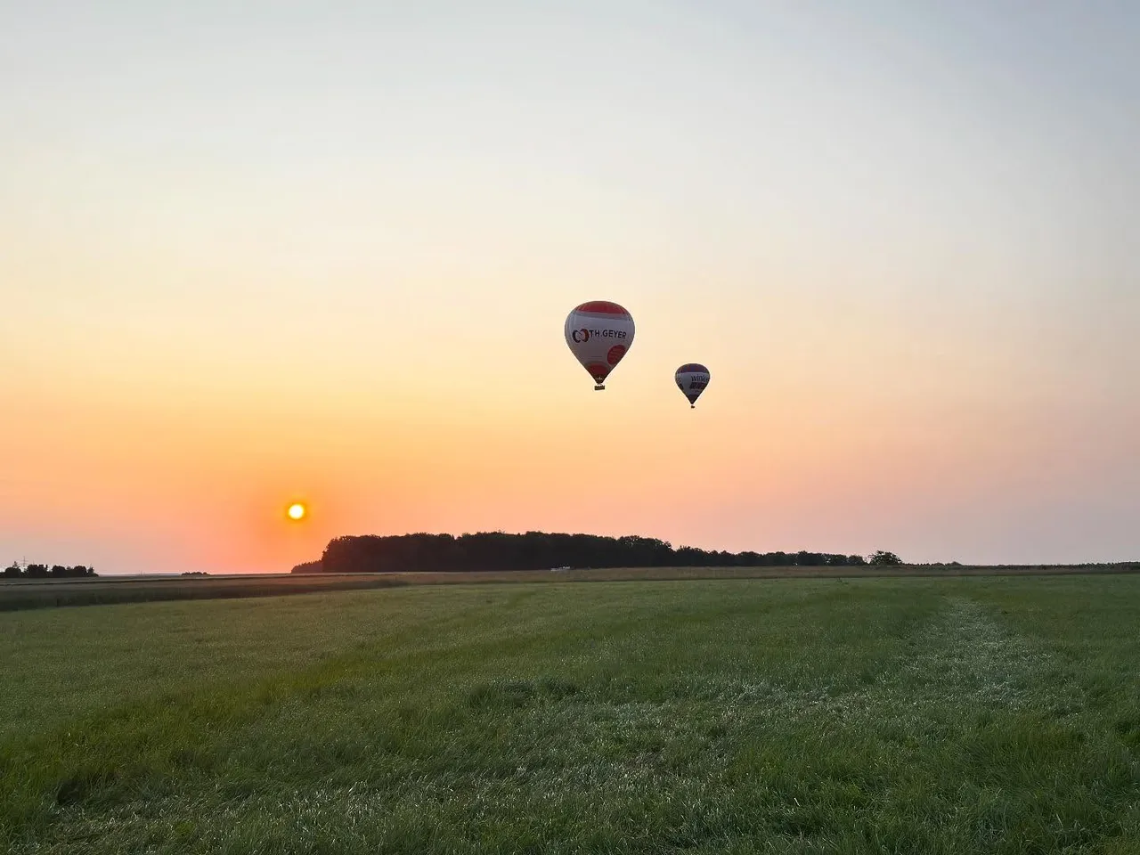 Two hot air balloons floating above a meadow at sunset