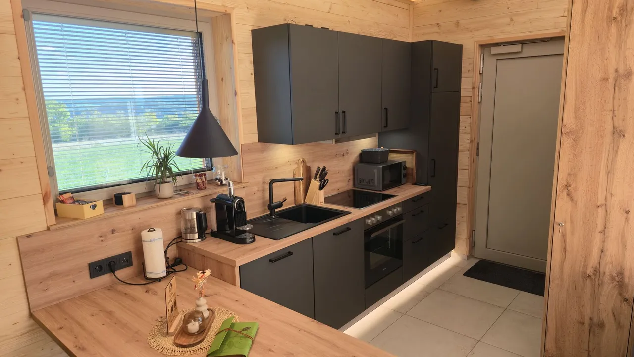 Fully equipped chalet kitchen with dark cabinets, wooden worktop, coffee machine and window with countryside view