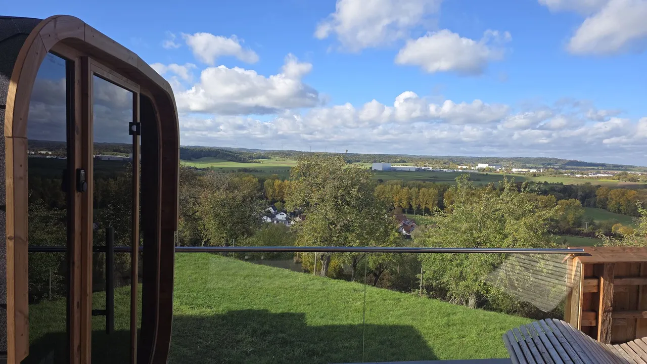 Outdoor sauna with glass door on a hillside terrace with panoramic view over autumn countryside