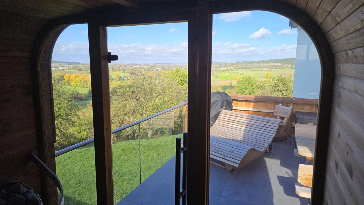 View from the sauna onto a private terrace with wooden sun lounger and wide autumn countryside