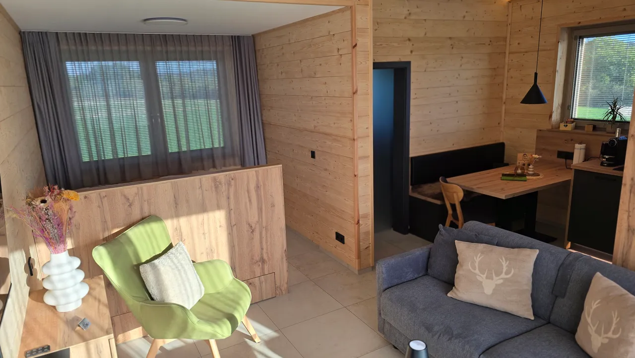 Cosy chalet living room with green armchair, grey sofa with deer cushions and wooden dining table