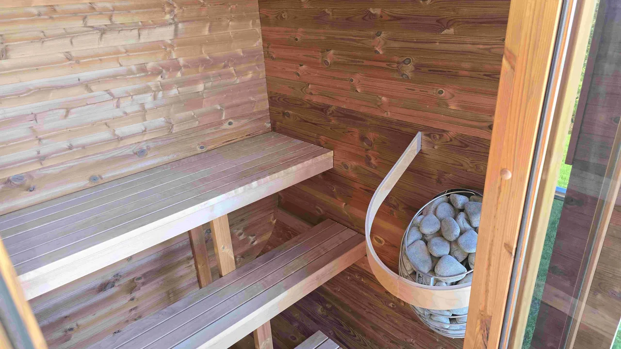 Interior of a wooden sauna with two benches and a sauna stove filled with stones