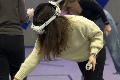 Woman wearing a VR headset bending down to grab a virtual object with her controller during a VR escape game
