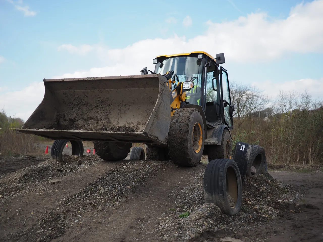 Person driving a yellow wheel loader over a dirt mound on an obstacle course with tires