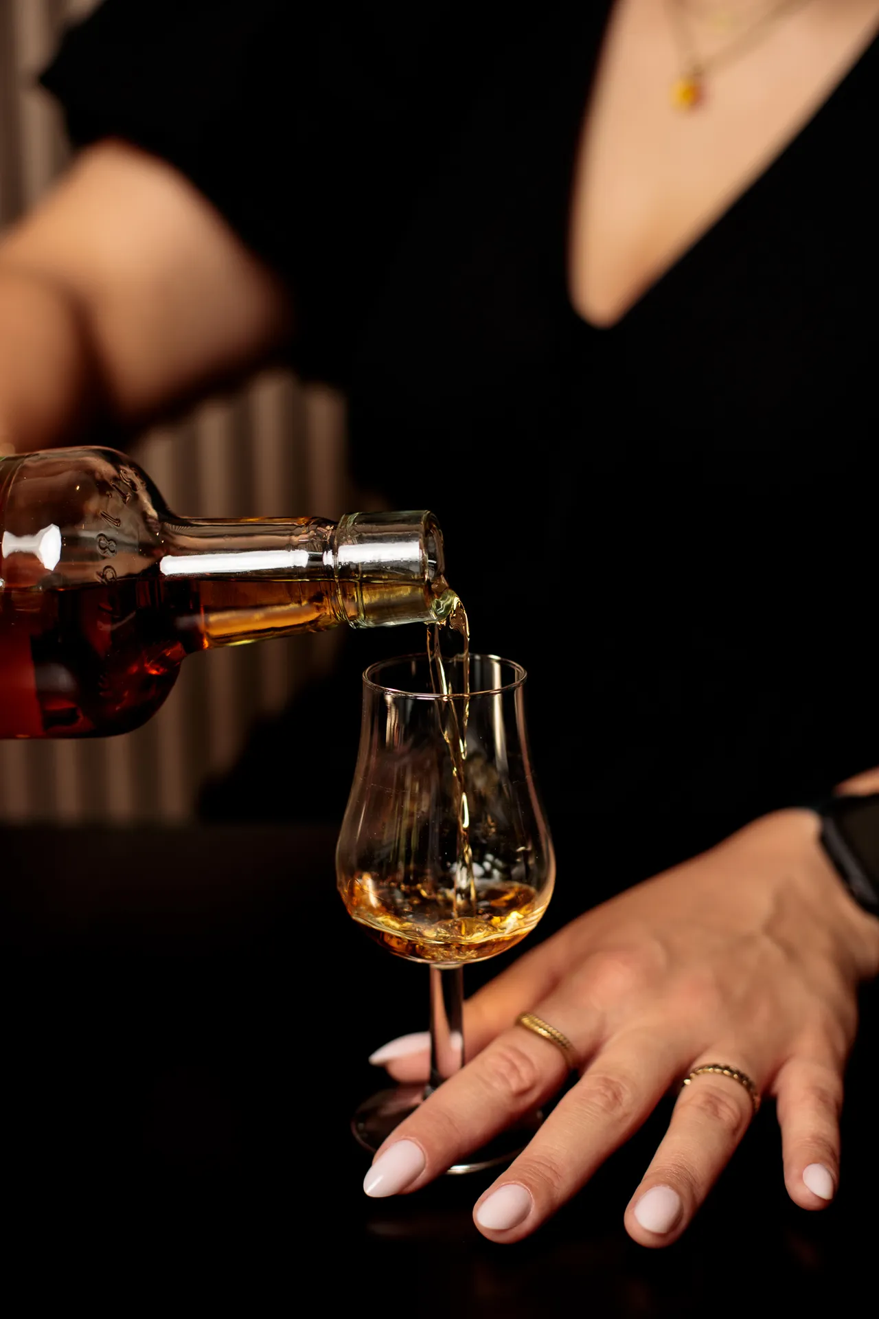 Whiskey being poured from a bottle into a nosing glass held by hand.
