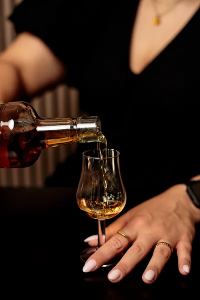 Whiskey being poured from a bottle into a nosing glass held by hand.