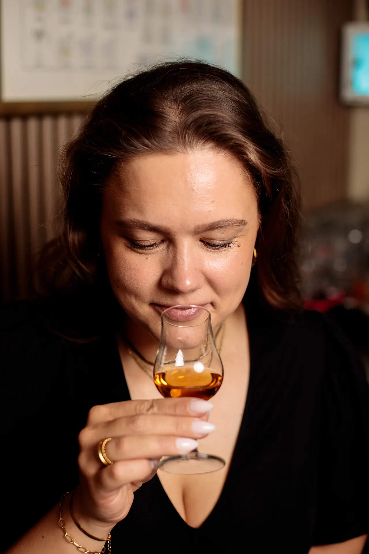 Close-up of a woman sipping whiskey from a tasting glass, savoring the flavor with her eyes lowered.