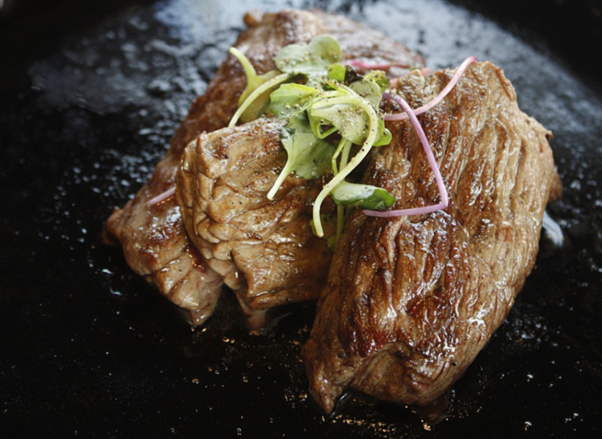 Seared venison medallions topped with fresh microgreens on a black cast-iron plate