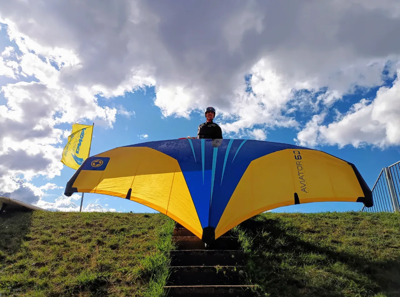 A person holding a yellow and blue hydrofoil for wingfoiling