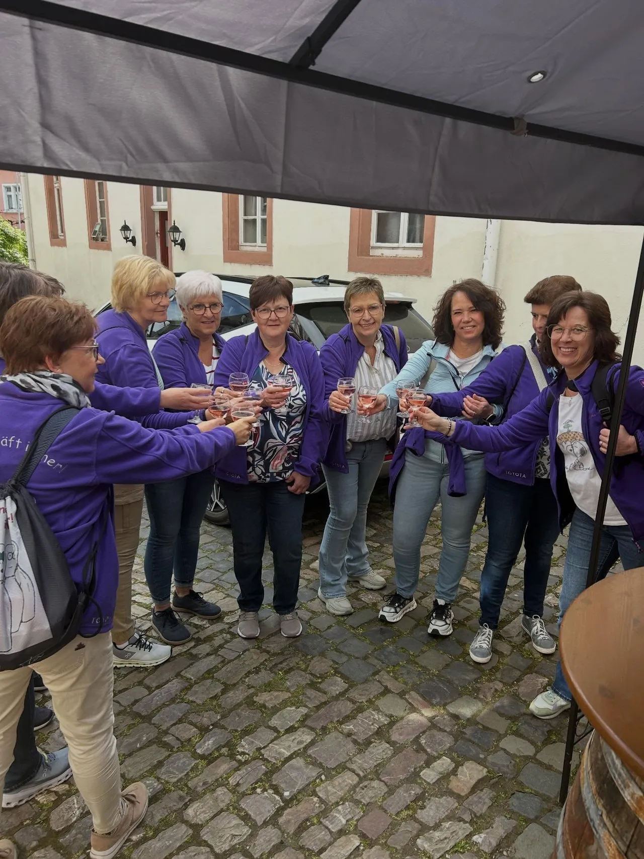 Group of women in matching purple fleece jackets toasting with rosé wine in a cobblestone courtyard during a guided wine tour.
